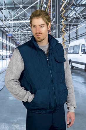 Homem com colete acolchoado azul escuro e sweatshirt cinza em armazém