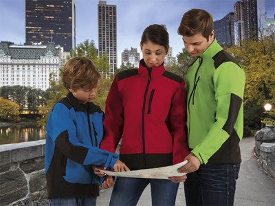 Três pessoas com casacos softshell coloridos numa paisagem urbana.