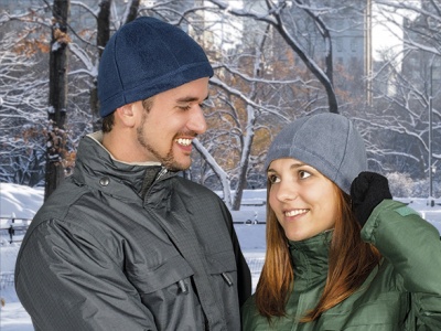 Homem e mulher com gorros de lã e casacos acolchoados num parque nevado