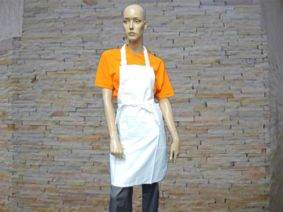 Manequim com camisa laranja e avental branco em frente a parede de pedra clara