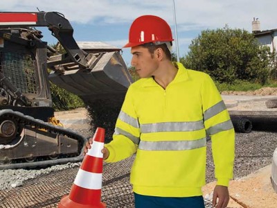 Trabalhador com colete amarelo e capacete vermelho segurando cone de sinalização num estaleiro