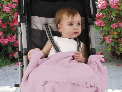 Bebé num carrinho preto e cinza coberto com manta rosa rodeado de flores.