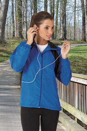 Mulher com casaco azul e auriculares ao ar livre num passadiço de madeira