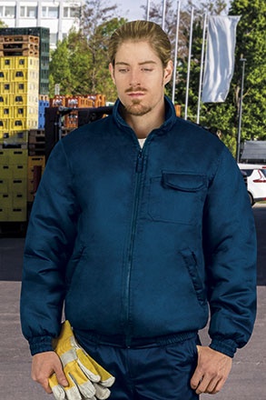 Homem com casaco azul escuro segurando luvas amarelas em ambiente industrial exterior