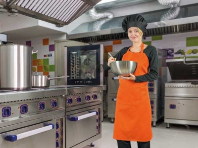 Cozinheira com avental laranja e chapéu preto em cozinha industrial