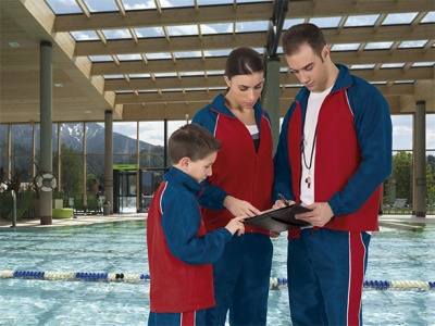 Três pessoas com fatos de treino vermelhos e azuis junto a piscina interior