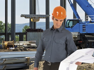 Homem com camisa cinza e capacete laranja em obra com guindaste