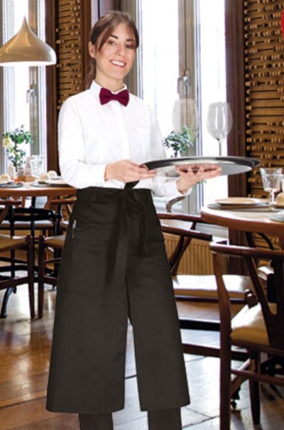 Garçonete com camisa branca, gravata borboleta vermelha e avental preto comprido num restaurante