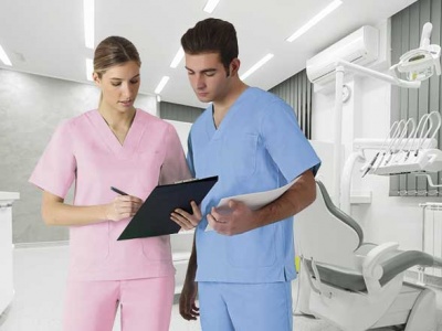 Dois profissionais de saúde com uniformes médicos rosa e azul em consultório dentário