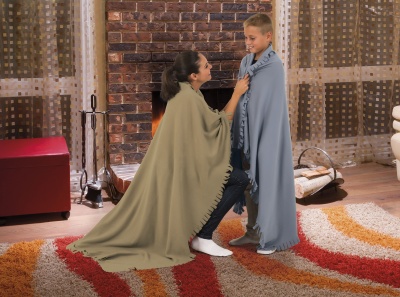 Mulher e criança com mantas bege e azul clara junto à lareira num ambiente acolhedor com tapete colorido e tijolos.