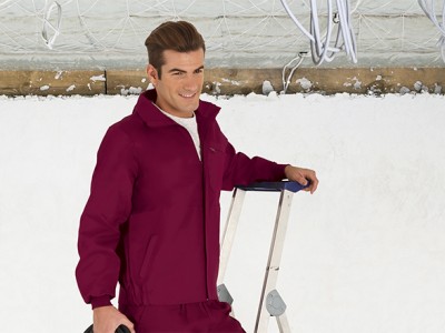 Homem com fato de trabalho bordeaux encostado numa escada metálica junto à neve