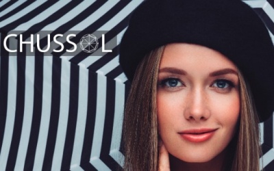 Mulher com boina preta e fundo listrado preto e branco com texto CHUSSOL