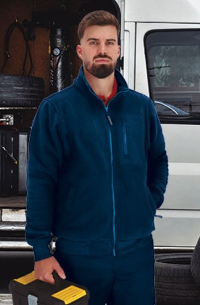 Homem com casaco polar azul escuro segurando caixa de ferramentas preta com tampa amarela em frente a carrinha branca