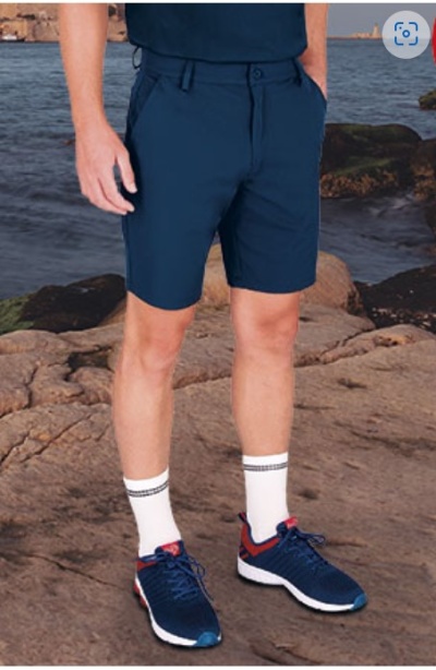 Homem com calções azuis e sapatilhas azuis em cima de rochas junto ao mar