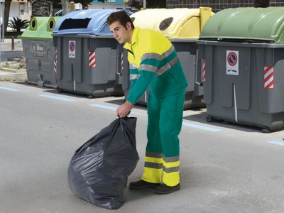 Homem com roupa de trabalho a segurar saco de lixo perto de contentores de reciclagem