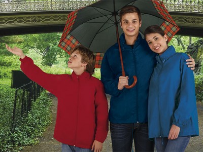 Três pessoas com casacos impermeáveis coloridos e um guarda-chuva xadrez em ambiente ao ar livre.