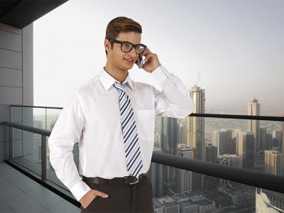 Homem de camisa branca e gravata a falar ao telefone num terraço com vista para cidade moderna