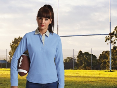 Mulher com polo azul segurando bola de futebol americano em campo de rugby