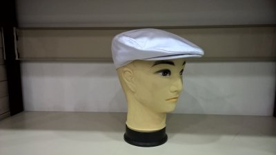 Boné tipo boina branco em manequim amarelo numa prateleira.