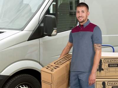 Homem com camisa polo cinza e bordô e calças cinza ao lado de caixas VALENTO DOUGH e carrinha branca