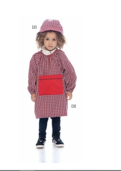 Criança com fato escolar xadrez vermelho e branco com avental e chapéu combinando, calças pretas e ténis no fundo branco