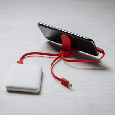 Suporte vermelho para smartphone com cabo USB e dispositivo branco em superfície clara