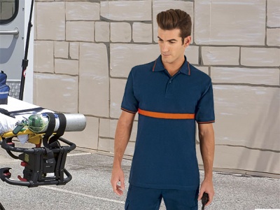 Homem com polo azul escuro e faixa laranja ao peito em rua com parede cinzenta