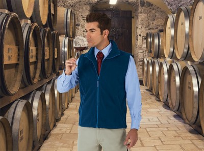 Homem a segurar taça de vinho numa adega com barris de madeira