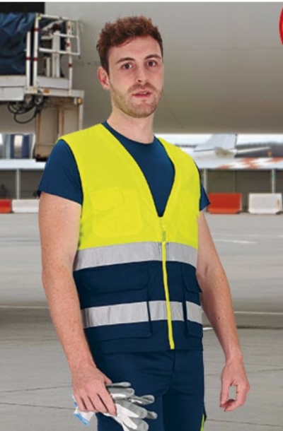 Homem com colete refletor amarelo e luvas de segurança num ambiente industrial