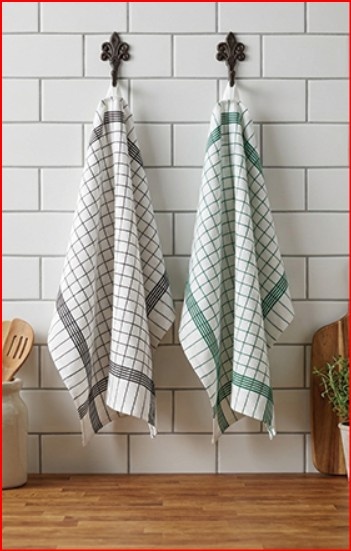 Duas toalhas de cozinha xadrez penduradas em ganchos numa parede de azulejos brancos