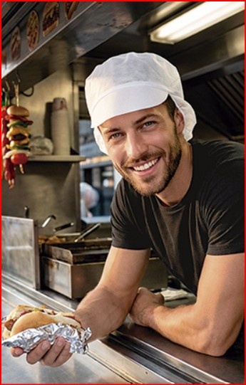Homem sorridente num food truck segurando hot dog embrulhado em papel alumínio