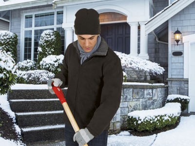 Homem com roupa de inverno a usar uma pá para neve em frente a casa com neve.