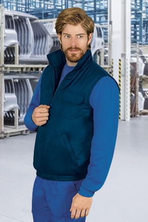 Homem com colete azul escuro e camisa azul em ambiente industrial