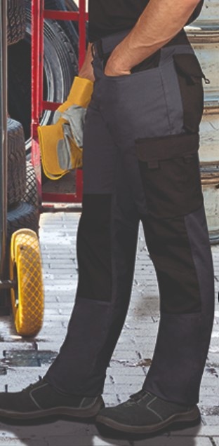 Calças de trabalho bicolores pretas e cinzentas com bolsos, pessoa segura luvas amarelas e cinzentas em ambiente de trabalho com pneus e carrinho.