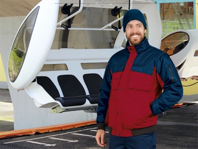 Homem com casaco azul e vermelho ao lado de teleférico branco