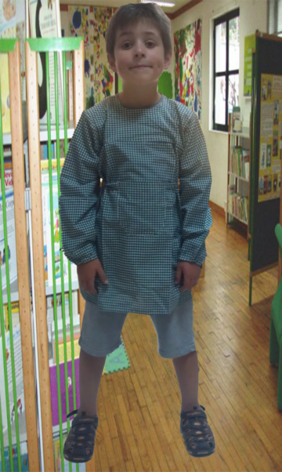 Criança com bata escolar verde em ambiente escolar interior.