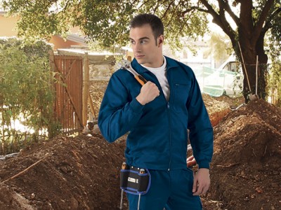 Homem com fato de trabalho azul e martelo ao ar livre junto a terra e vedação