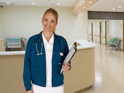 Enfermeira sorridente com jaleco azul e estetoscópio em corredor de hospital