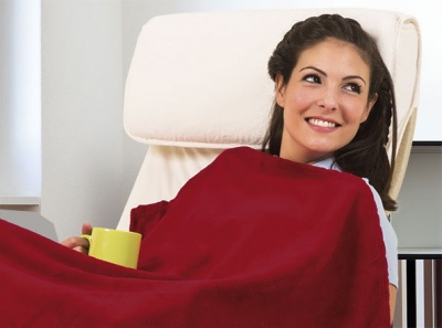 Mulher sorridente sentada numa cadeira branca com uma manta vermelha e uma caneca amarela