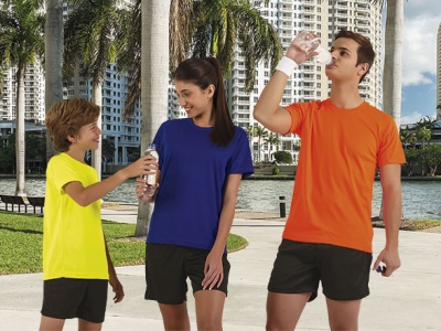 Três jovens ao ar livre com t-shirts coloridas e calções pretos junto a palmeiras e edifícios.