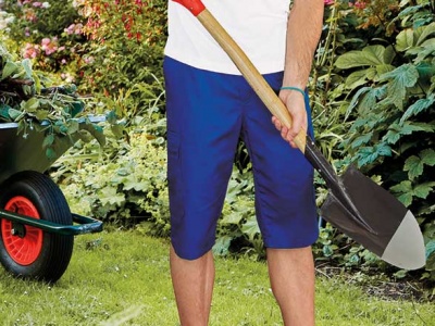 Pessoa com calções azuis segurando pá num jardim com relva e plantas