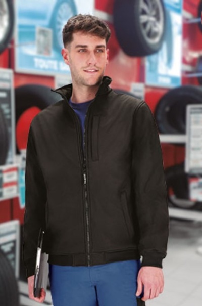 Homem com casaco preto e calças azuis num ambiente de oficina com pneus ao fundo