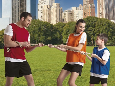 Homem, mulher e criança a jogar cabo de guerra em campo verde com coletes coloridos