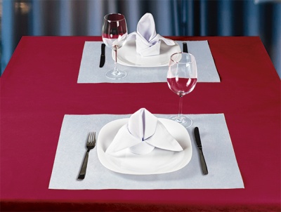 Mesa ajustada com toalha vermelha, pratos e guardanapos brancos, talheres pretos e copos de vinho