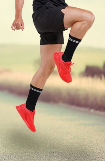 Pessoa a saltar usando ténis vermelhos, meias pretas e calções pretos numa estrada ao ar livre