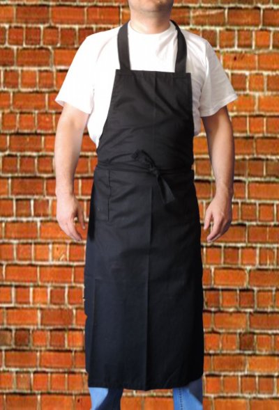 Homem a usar avental preto comprido com alças e cinto, fundo de tijolos vermelhos