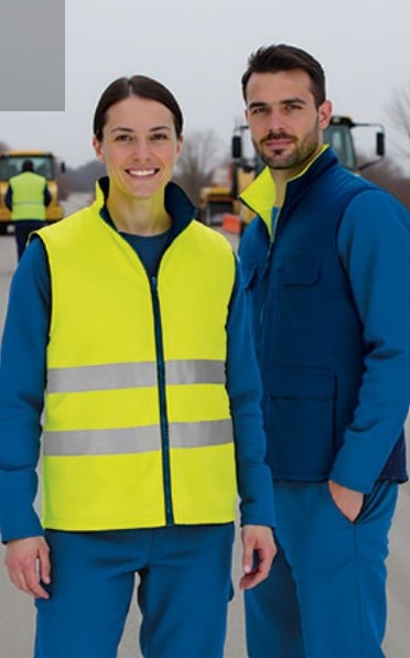 Duas pessoas com uniformes azuis, uma com colete amarelo fluorescente e faixas refletoras, em ambiente de trabalho externo