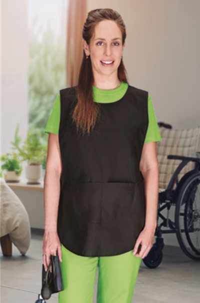 Pessoa com bata preta sobre roupa verde em ambiente interior com cadeira de rodas