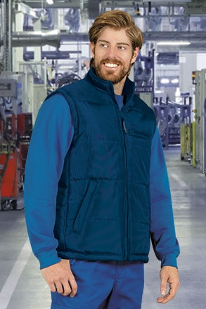 Homem com colete azul escuro acolchoado e camisa azul em ambiente industrial