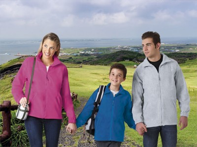Pessoa com casaco fleece rosa, criança com casaco azul e homem com casaco cinza num campo verde com vista para o mar